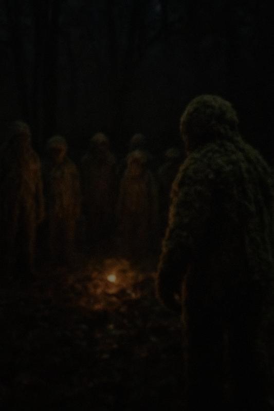 Mooslinge im Bild: Ein dunkles, leicht verwackeltes Bild einer Kultstätte der Moosinge. Etwas zehn Mooslinge sind auf dem Bild als Silhouetten erkennbar.