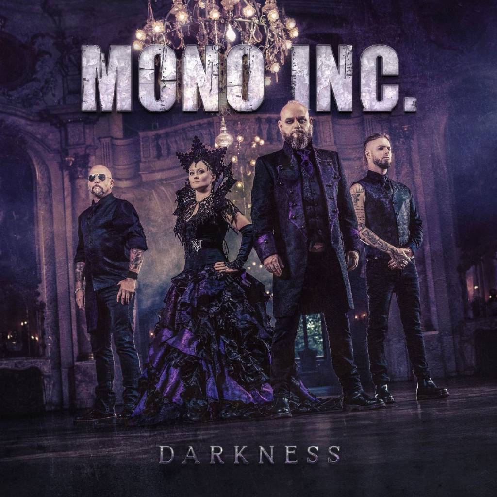 Die Band Mono Inc. steht in opulenten schwarz-violetten Gewändern in einem prunkvollen Ballsaal, die Kronleuchter glitzern – dramatische Gothic-Ästhetik trifft aristokratische Dunkelheit.