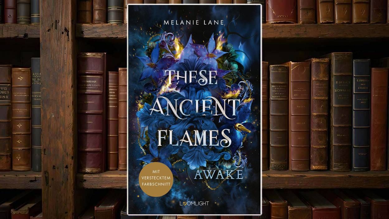 Cover von These Ancient Flames 1: Awake von Melanie Lane: Üppiges, dunkles Fantasy-Cover mit blauen Lilien, goldenen Flammenakzenten und filigranen Ornamenten. Titel in Silberprägung, unten Hinweis „mit verstecktem Farbschnitt“.