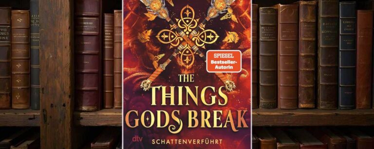 Cover von Abigail Owens »The Things Gods Break – Schattenverführt« vor einem Bücherregal: Auf feurig rotem Hintergrund kreuzen sich vier reich verzierte Speere um ein goldenes Ornament, darum schweben kleine mythische Symbole. Oben stehen der Autorenname und der Claim „Ihre Liebe: endlos. Ihr Gegner: die Zeit selbst“, unten prangt der Titel in großen goldenen Lettern mit dem Untertitel „Schattenverführt“ und einem orangefarbenen SPIEGEL-Bestseller-Sticker.