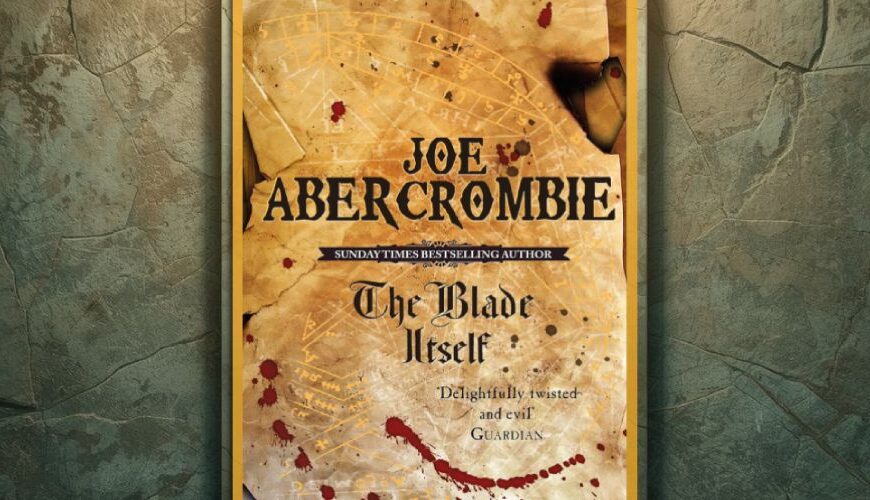 Vor einer rissigen, moosig wirkenden Steinwand hängt das Cover von Joe Abercrombies The Blade Itself in einem goldenen Rahmen. Die Gestaltung zeigt Pergamentoptik, feine Linien wie eine Karte und rote Blutspritzer, wodurch das Motiv wie ein ausgestelltes Relikt wirkt.