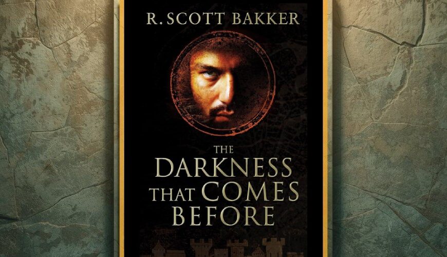 Buchcover von „The Darkness That Comes Before“ von R. Scott Bakker im goldenen Rahmen vor einer verwitterten Steinwand; im Zentrum ein düsteres Gesicht im Kreis aus Symbolen.