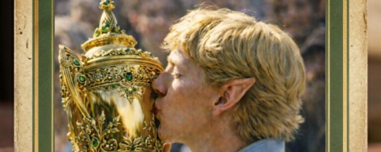 Analoge Fantasy-Sportfotografie im Hochformat: Ein blonder Hochelf mit spitzen Ohren und himmelblauer, goldbestickter Zeremonien-Sportkleidung küsst einen prunkvollen goldenen Pokal mit grünen Edelsteinen. Im Hintergrund verschwimmt die Menge wie bei einem historischen Turniermoment.