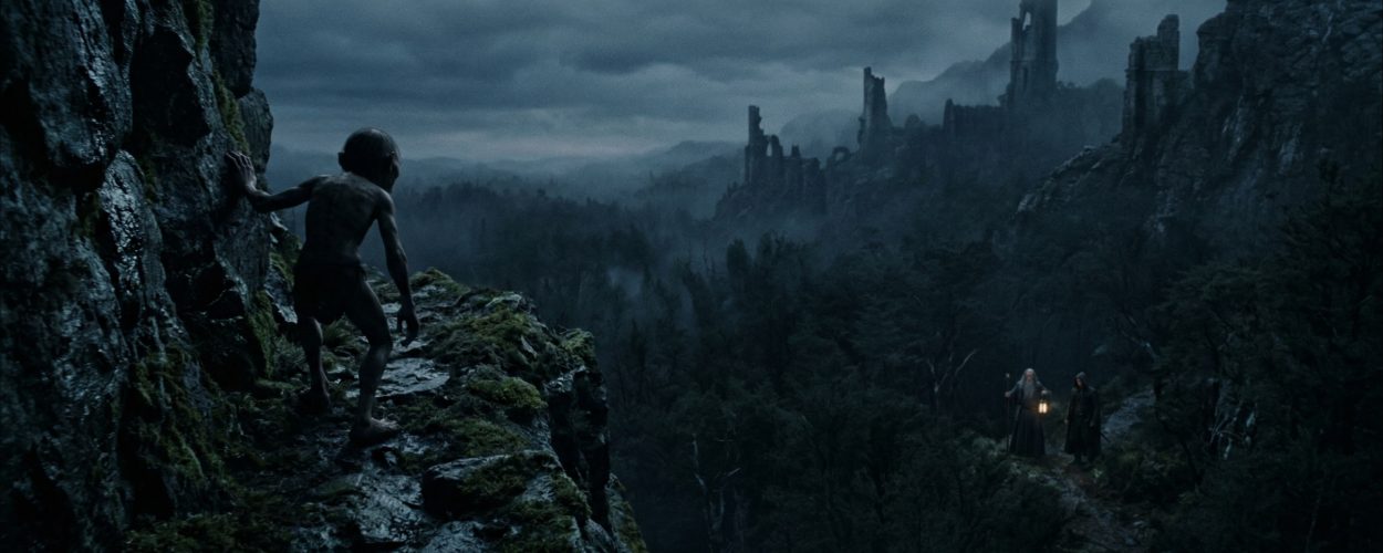Eine zerlumpte Gestalt schleicht an einem moosigen Felsweg entlang, während in der Ferne Suchende mit Laternen durch einen nebligen Wald ziehen – Symbolbild zu The Hunt for Gollum.