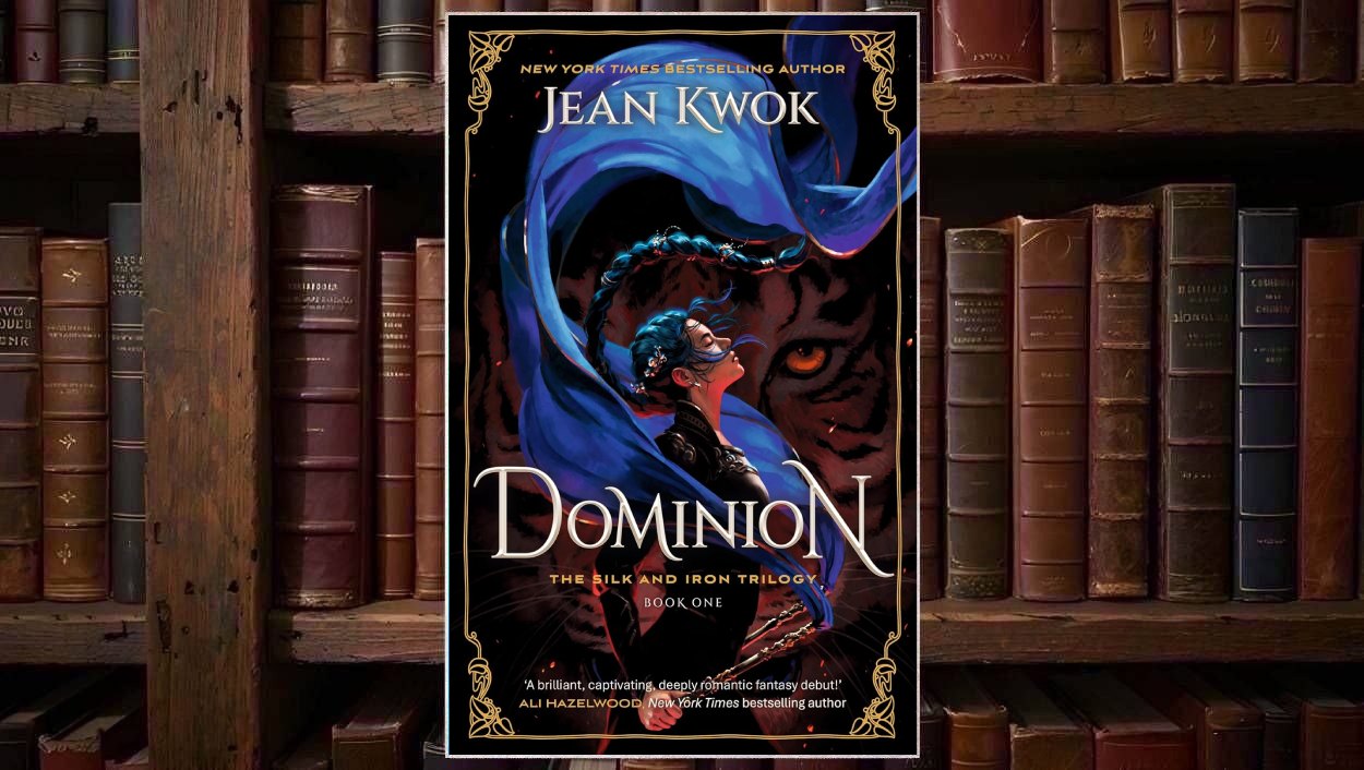 Cover von Jean Kwoks Dominion mit einer dunkelhaarigen Kriegerin, die von langen blauen Stoffbändern umkreist wird, vor dem gewaltigen Gesicht eines orangeäugigen schwarzen Tigers und einem goldenen ornamentalen Rahmen.