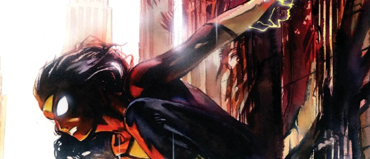 Spider-Woman kauert an einer Hochhausfassade in New York. Ihre schwarzen Haare wehen nach hinten, während gelbe Energie um ihre Hände leuchtet und sich ihr rot-schwarz-gelbes Kostüm vor der dunklen Hauswand abhebt.