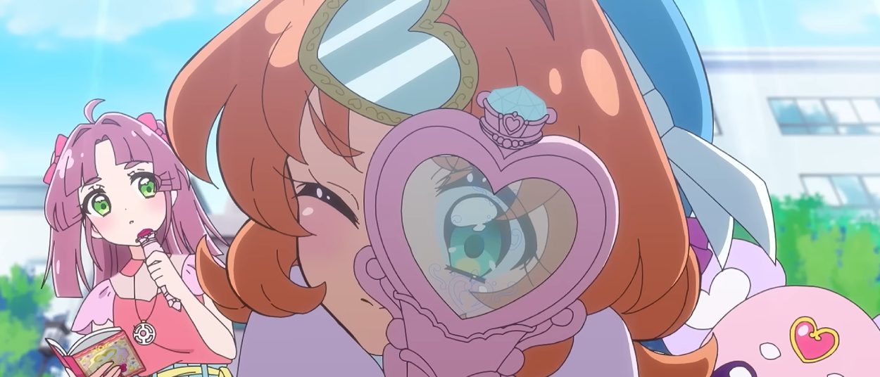 Eine orangehaarige Anime-Figur hält einen herzförmigen Spiegel vor ihr Auge, während hinter ihr eine pinkhaarige Figur mit einem Buch und ein kleines rosafarbenes Wesen zu sehen sind.