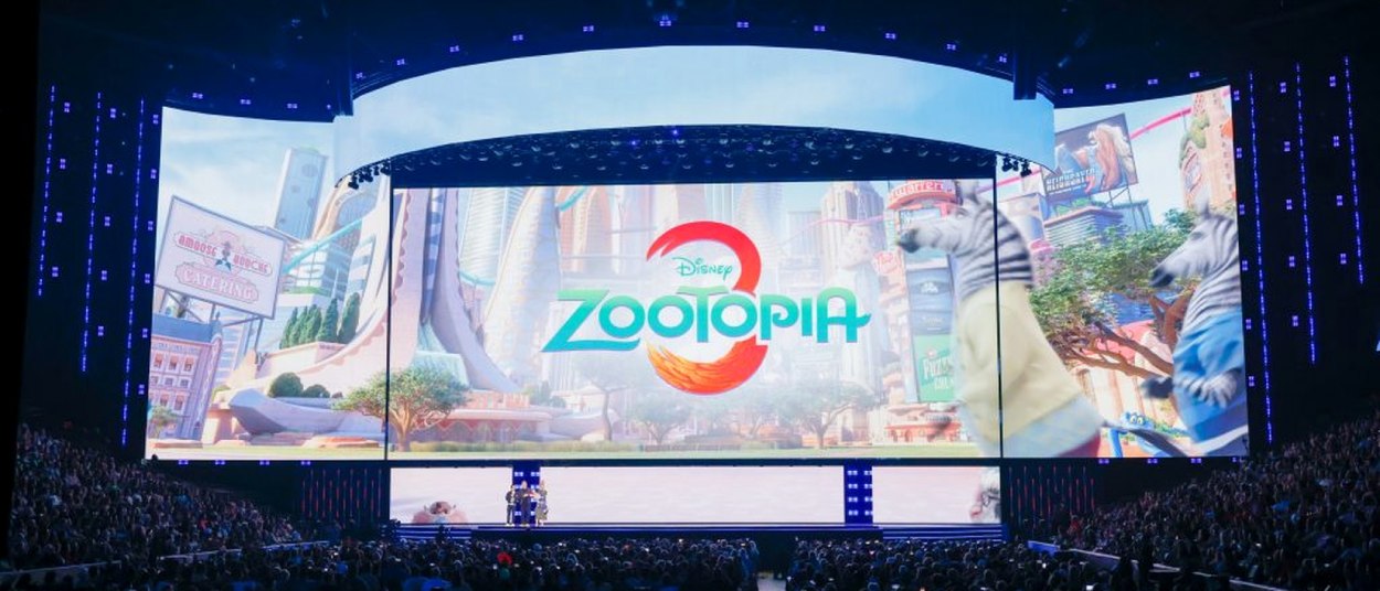 Eine große Bühne auf der Disney-Messe D23 zeigt auf einer breiten Leinwand das farbige Logo von Zootopia 3 vor einer Stadtkulisse; davor sitzt ein großes Publikum.