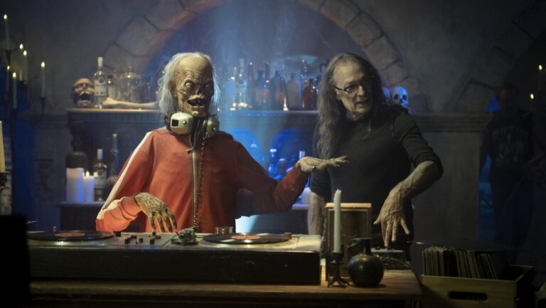 Der neu gestaltete Crypt Keeper steht mit Kopfhörern hinter Plattenspielern in einer düsteren Gruftkulisse, während neben ihm an der Szenerie gearbeitet wird.
