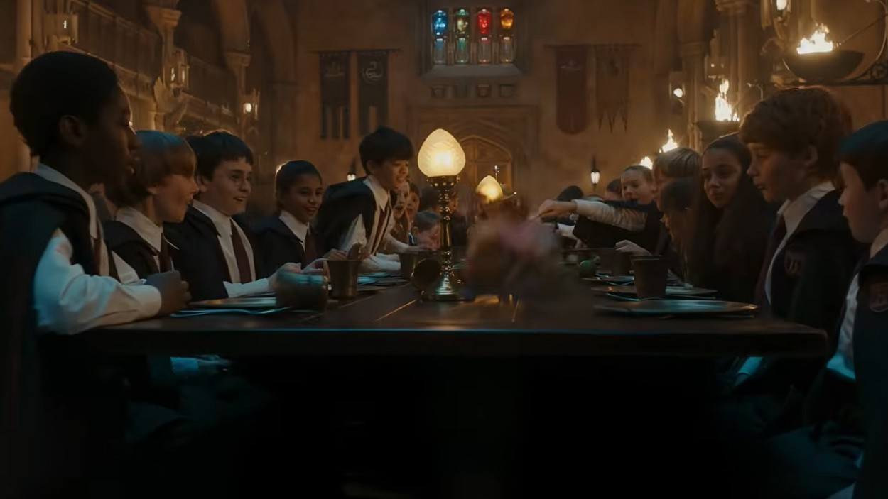 Schüler sitzen in der Großen Halle von Hogwarts an langen Tischen, während über der Tafel eine magische Szene für Aufsehen sorgt.