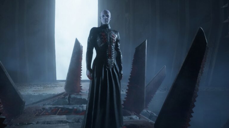 Pinhead steht in Clive Barker’s Hellraiser: Revival in einer düsteren Labyrinthkammer zwischen großen gezackten Metallstrukturen.