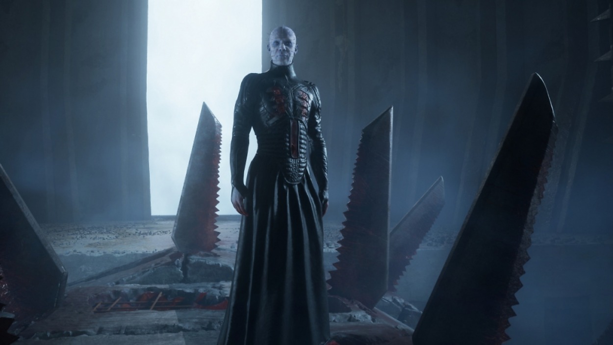 Pinhead steht in Clive Barker’s Hellraiser: Revival in einer düsteren Labyrinthkammer zwischen großen gezackten Metallstrukturen.