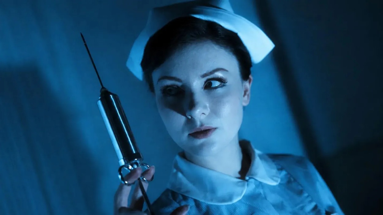 Eine Krankenschwester hält in blauem Licht eine übergroße Spritze hoch und blickt angespannt zur Seite.