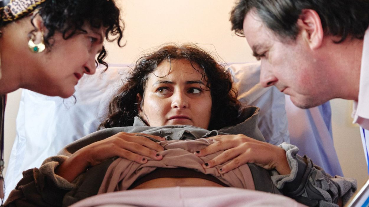 Mary liegt schwanger in einem Krankenhausbett, während ihre Mutter und ein Arzt sie im Science-Fiction-Horrorfilm Mum, I’m Alien Pregnant untersuchen.