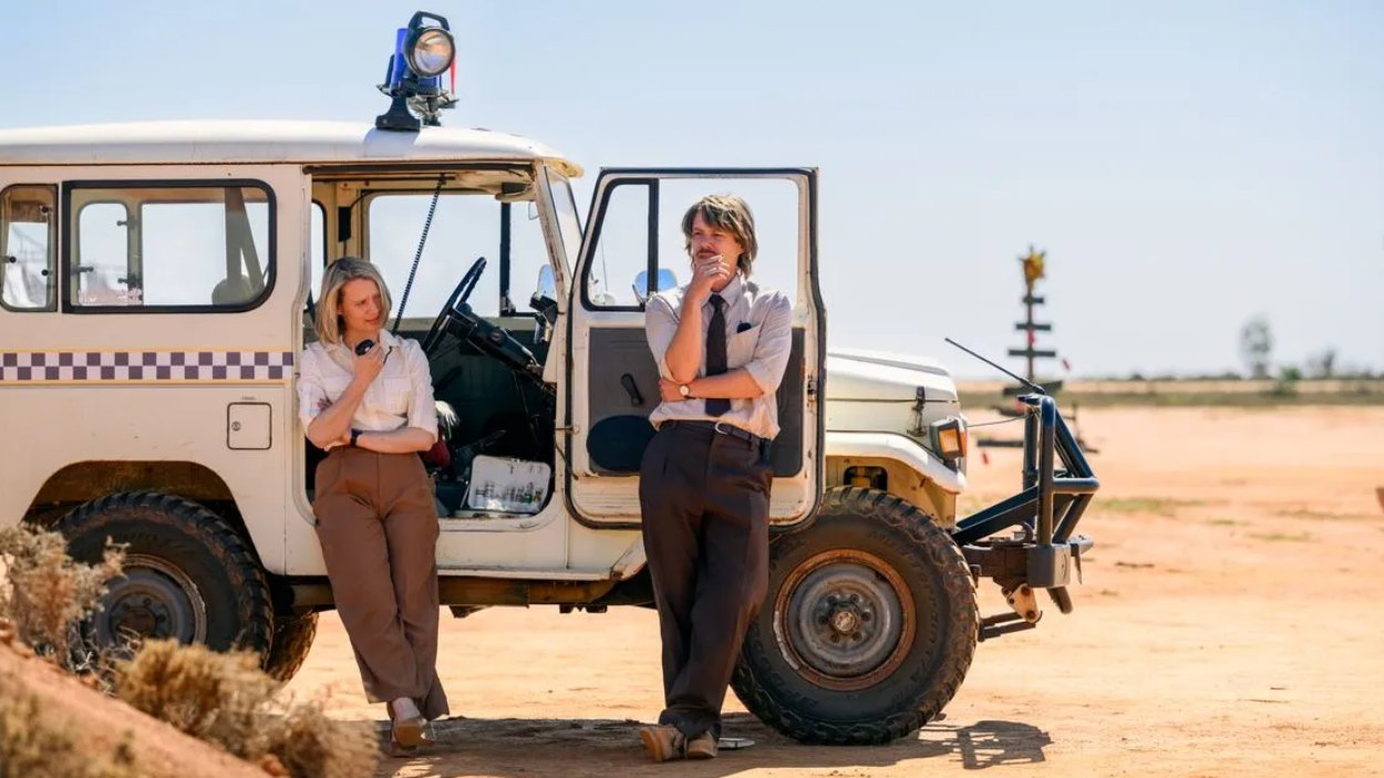 Zwei Ermittler stehen neben einem Geländewagen in einer abgelegenen, trockenen Outback-Landschaft aus The Killings: Parrish Station.