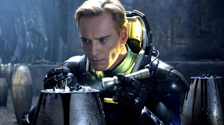 Filmszene aus Prometheus: Ein blondhaariger Mann in einem dunklen futuristischen Schutzanzug untersucht konzentriert einen geheimnisvollen metallischen Behälter. Kaltes blaues Licht und eine düstere außerirdische Umgebung prägen die Szene.