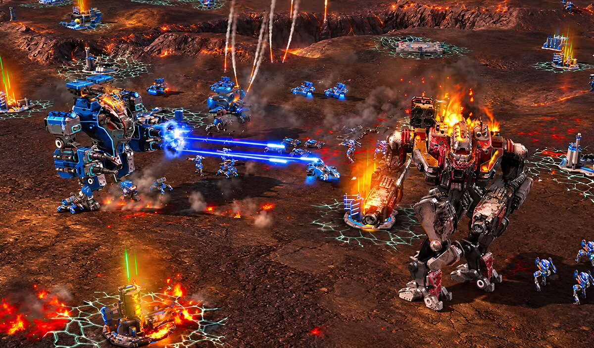 Zwei gewaltige futuristische Kampfroboter stehen sich auf einem brennenden, felsigen Schlachtfeld gegenüber. Ein blauer Mech feuert Energiestrahlen auf einen rot gepanzerten Gegner, während zahlreiche kleinere Einheiten kämpfen.
