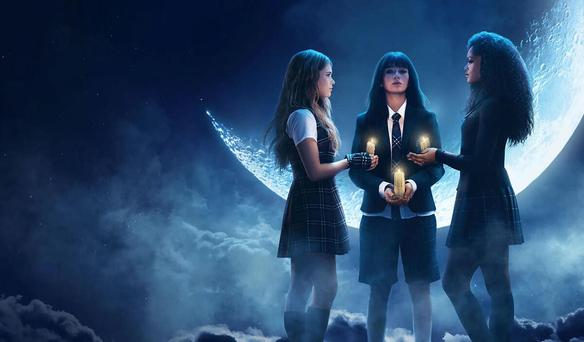 Offizielles Serienmotiv zu Coven Academy. Drei junge Hexenschülerinnen in dunklen Schuluniformen stehen in einem Kreis und halten brennende Kerzen. Hinter ihnen leuchtet ein gewaltiger bläulicher Mond. Dichter Nebel, Wolken und kaltes Mondlicht verleihen der Szene eine geheimnisvolle Atmosphäre.