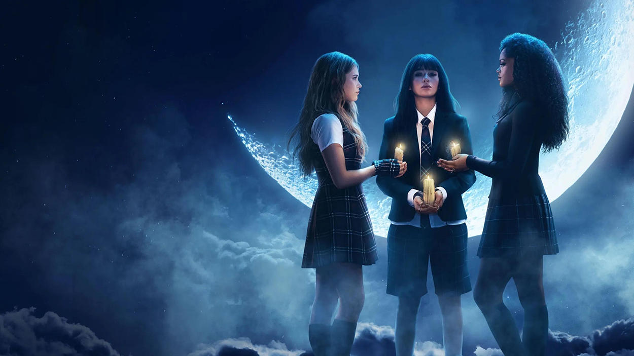 Offizielles Serienmotiv zu Coven Academy. Drei junge Hexenschülerinnen in dunklen Schuluniformen stehen in einem Kreis und halten brennende Kerzen. Hinter ihnen leuchtet ein gewaltiger bläulicher Mond. Dichter Nebel, Wolken und kaltes Mondlicht verleihen der Szene eine geheimnisvolle Atmosphäre.