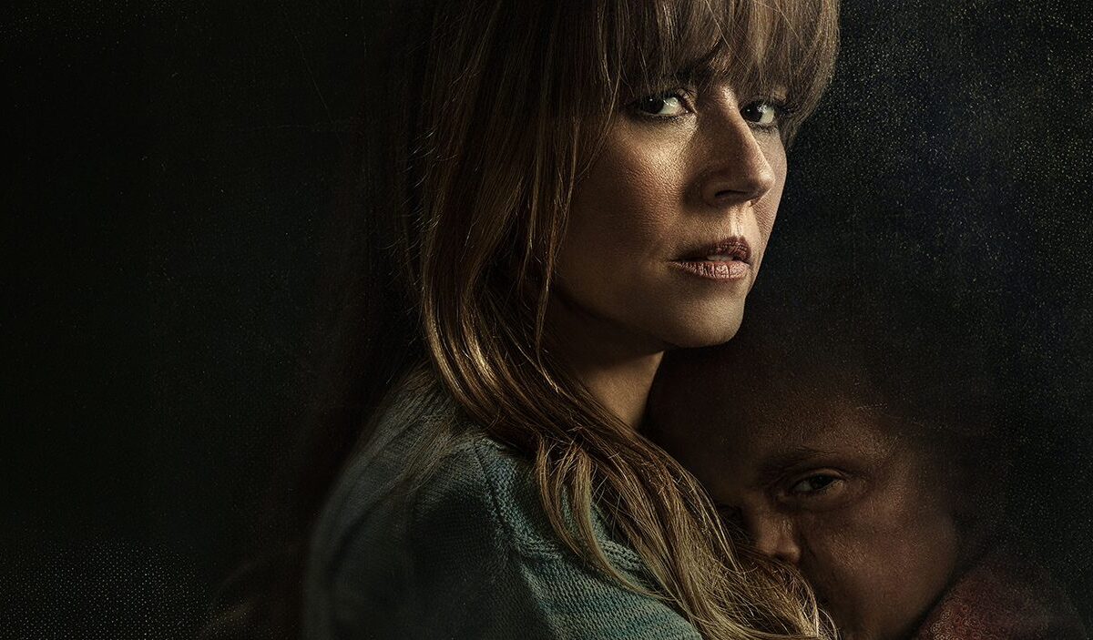 Eine ernst blickende Frau mit langen braunen Haaren hält einen kleinen Jungen eng an sich. Beide stehen vor einem fast schwarzen Hintergrund im düsteren Promomotiv der Horrorserie Crystal Lake.