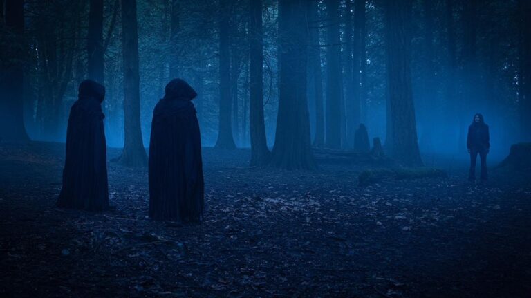 Mehrere dunkel gekleidete Gestalten stehen in einem nächtlichen, blau beleuchteten Wald einer einzelnen Frau gegenüber.