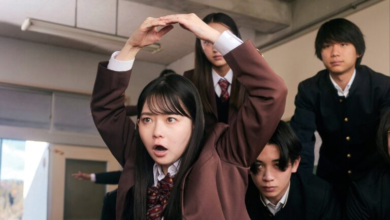 Eine japanische Schülerin hebt in New Group während einer Turnübung die Arme über den Kopf, während mehrere Mitschüler sie aufmerksam beobachten.