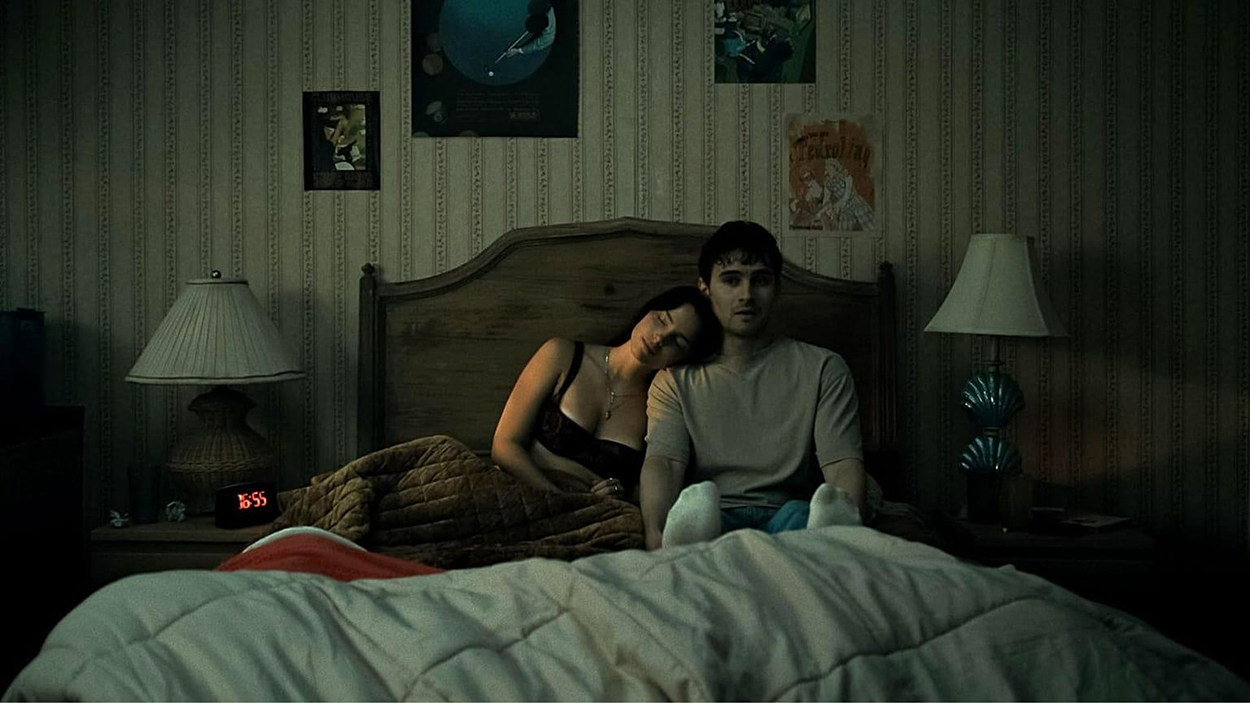 Düstere Schlafzimmerszene aus dem Horrorfilm Obsession von Curry Barker. Eine dunkelhaarige Frau lehnt mit geschlossenen Augen an der Schulter eines jungen Mannes, der mit starrem, ausdruckslosem Blick auf einem Bett sitzt. Gedämpftes grünliches Licht und altmodische Tapeten erzeugen eine beklemmende Atmosphäre.