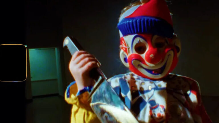 Unheimliche Gestalt mit rot-weiß-blauer Clownsmaske und großem Messer in einem dunklen Raum. Das körnige Filmbild aus Project Shamrock wirkt wie eine beschädigte Archivaufnahme aus den 1960er-Jahren.