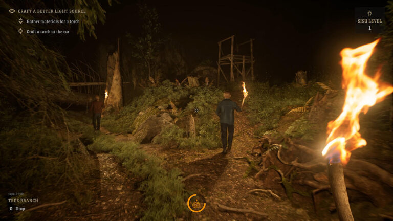 Gameplay-Screenshot aus RAHKO: Shadows Around Us: Zwei Spielfiguren laufen mit brennenden Fackeln durch einen dunklen Wald. Im Vordergrund ist die Fackel des Spielers zu sehen. Felsen, Büsche und ein hölzerner Hochstand liegen im schwachen Feuerschein.