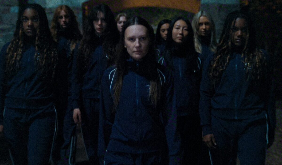 Eine Gruppe junger Frauen in dunklen Trainingsanzügen steht nachts dicht zusammen und blickt ernst nach vorn.