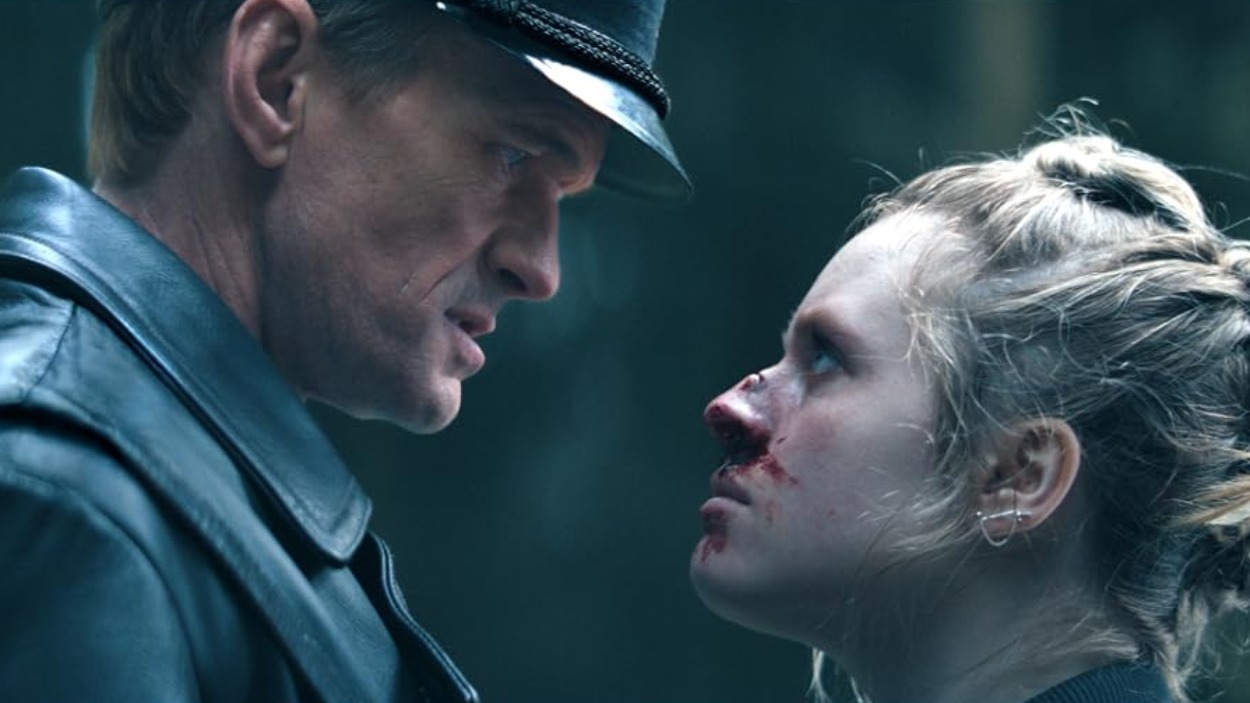 Verletzte junge Frau steht einem bedrohlichen Mann in dunkler Uniform gegenüber in The Last Temptation of Becky.