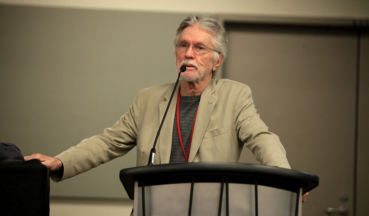 Tom Skerritt mit grauem Haar, Bart und beigem Sakko spricht bei einer Veranstaltung im Dezember 2014 hinter einem Rednerpult in ein Mikrofon.