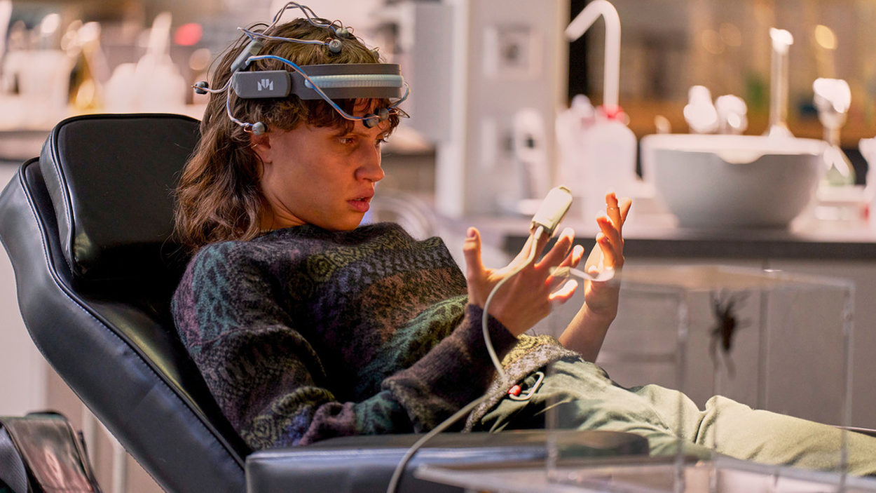 Luna Jordan als Emilia in der ZDF-Science-Fiction-Serie Wake Up: Mit einem technischen Gerät am Kopf sitzt sie in einem Behandlungsstuhl und betrachtet verwundert ihre Hände, während Hevis Bewusstsein ihren Körper kontrolliert.