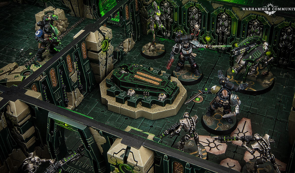 Tabletop-Spielfeld aus Warhammer 40.000: Kill Team mit bemalten Deathwatch-Space-Marines und Necron-Kriegern zwischen hohen Mauern und Deckungen einer grün beleuchteten Tomb-World-Gruftwelt.
